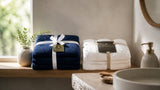 Folded navy blue and white cotton bath towels on a light oak bathroom shelf