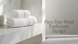 Folded white 700 GSM cotton towel set and a silver grey bath rug styled in a premium hotel-style bathroom setting
