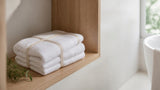 Stack of folded white cotton bath towels on a light oak bathroom shelf