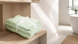 Folded sage green cotton towel set on a light oak bathroom shelf