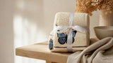Folded cream cotton embroidered butterfly towel set tied with a ribbon on a light wooden bathroom shelf