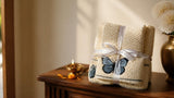 Folded embroidered butterfly cotton towel set tied with a white ribbon beside a brass diya on a wooden console