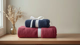 Folded navy blue and burgundy cotton towels on a wooden bathroom shelf beside a window
