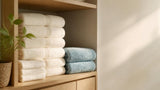 Willow and Fern folded cotton towel set and blue bath rug neatly stacked on a wooden shelf