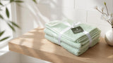 Folded sage green cotton bath towel set tied with a ribbon on a light wooden bathroom shelf