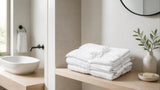 Folded white cotton towels tied with a ribbon on a light wood bathroom shelf