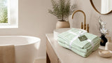Folded sage green Willow & Fern towel set tied with ribbon on a bathroom vanity beside a freestanding tub