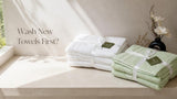 Folded white and sage green cotton towel sets on a pale stone shelf in soft morning light
